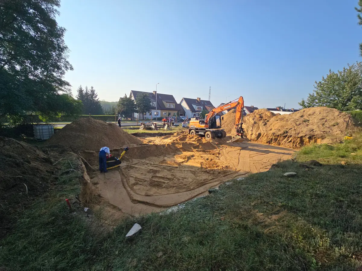 Koparka przy wykopie pod płytę fundamentową domu, w tle domy jednorodzinne