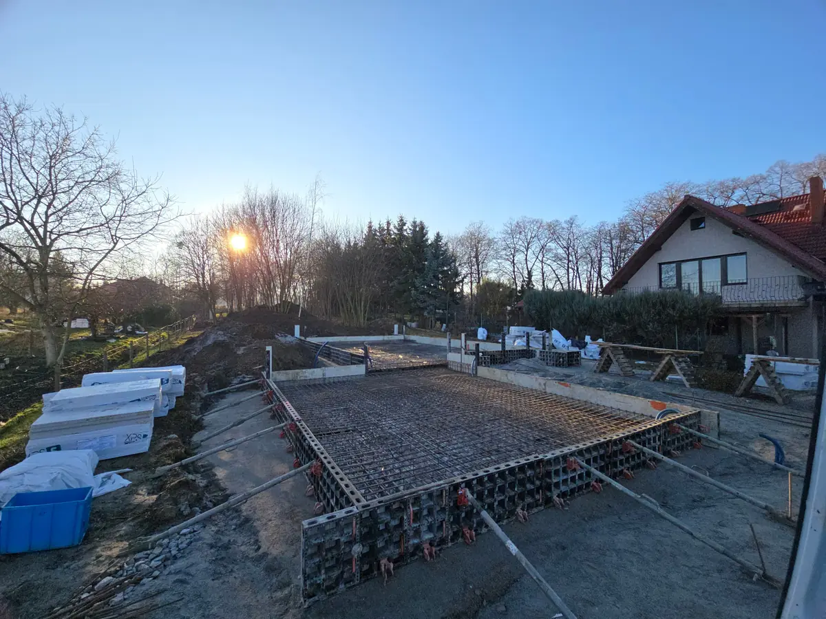 Zbrojenie płyty fundamentowej w szalunku systemowym, w tle dom jednorodzinny